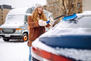 Woman brusshing snow and ice off of her car windows